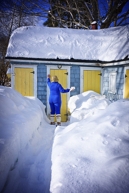 成熟的女人在冬天的雪地里走向户外厕所。