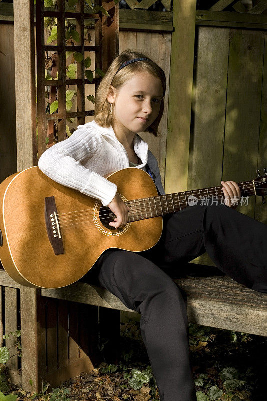 一个小女孩在外面的长椅上弹吉他。