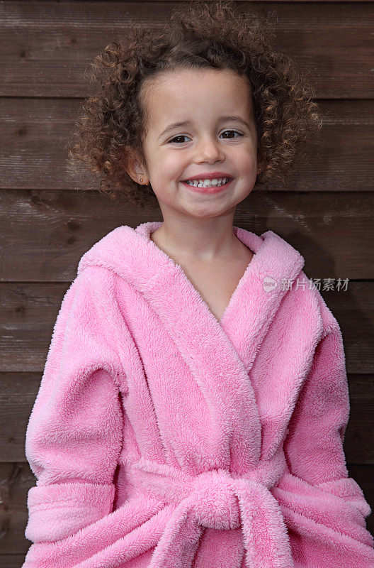 微笑的女孩，一头棕色的卷发，穿着粉红色的浴袍