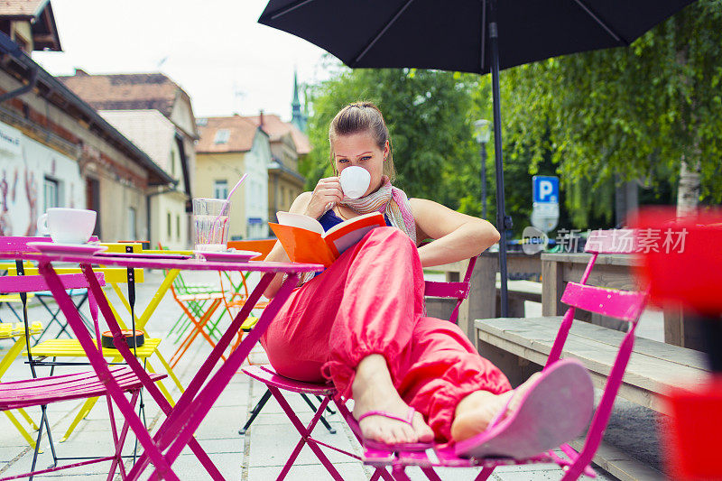时髦的年轻女孩坐在和阅读在欧洲户外咖啡馆