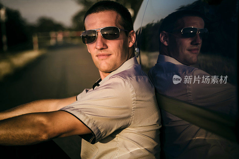 夕阳西下，年轻人坐在汽车旁