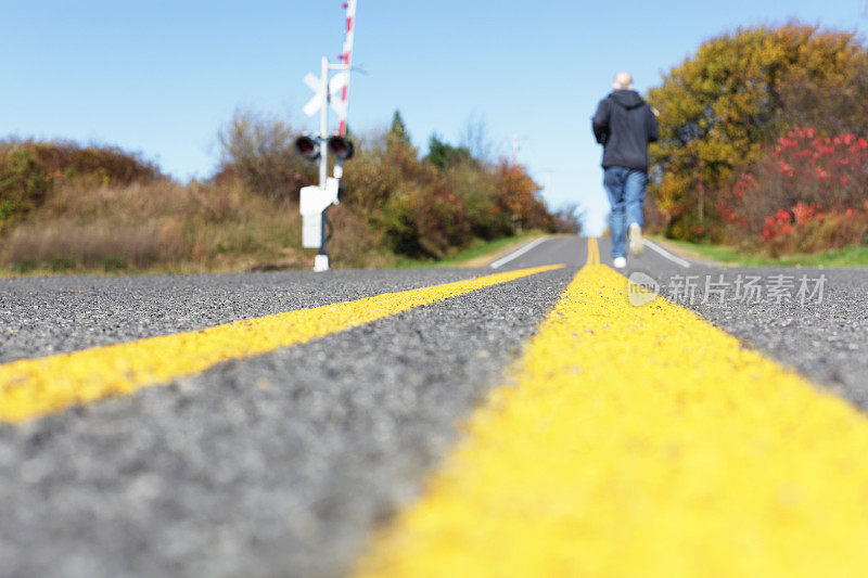 穿过铁路轨道的黄线乡村公路上的跑步者