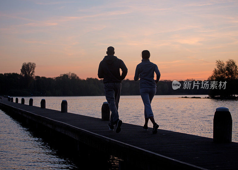 一对夫妇在黎明时分在湖上跑步的剪影