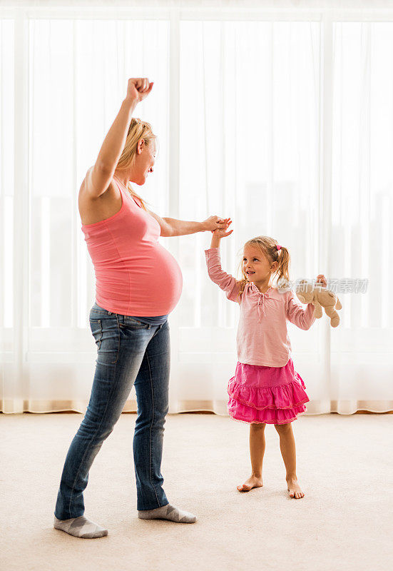 快乐的怀孕母亲在家里和女儿跳舞。