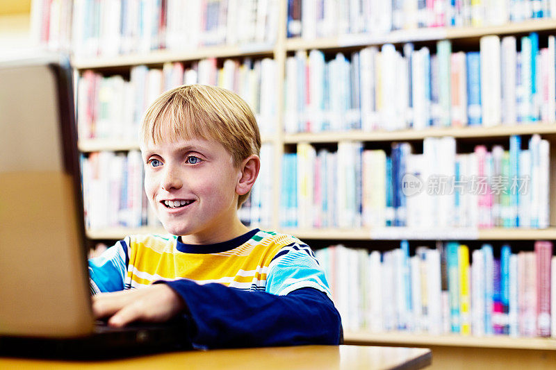 微笑的金发男孩上网在图书馆设置