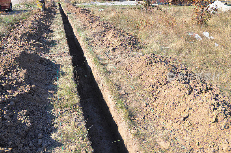 挖沟。土方工程,挖战壕。为铺设管道或光纤而挖的长土沟。