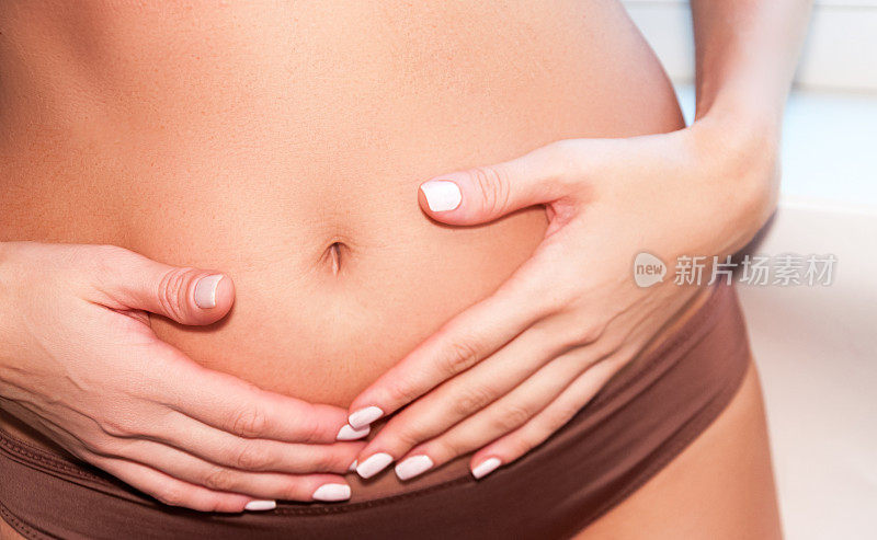 一个晒黑了的女孩把手放在肚子上。体外受精概念、妊娠、消化、女性生殖系统健康。