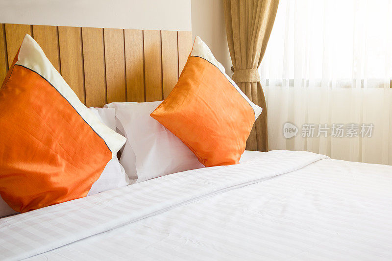 卧室床上橙色枕头和白色毯子，右上方有灯光