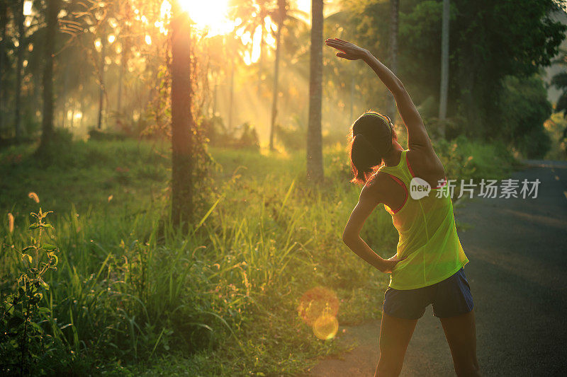 年轻的女性跑步者在晨跑前热身森林小径