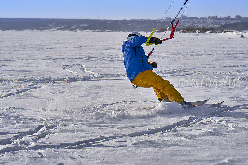 一个男运动员正在一个大的雪湖上的冰上放风筝。他在雪地里滑雪。冬天晴朗有霜的一天。