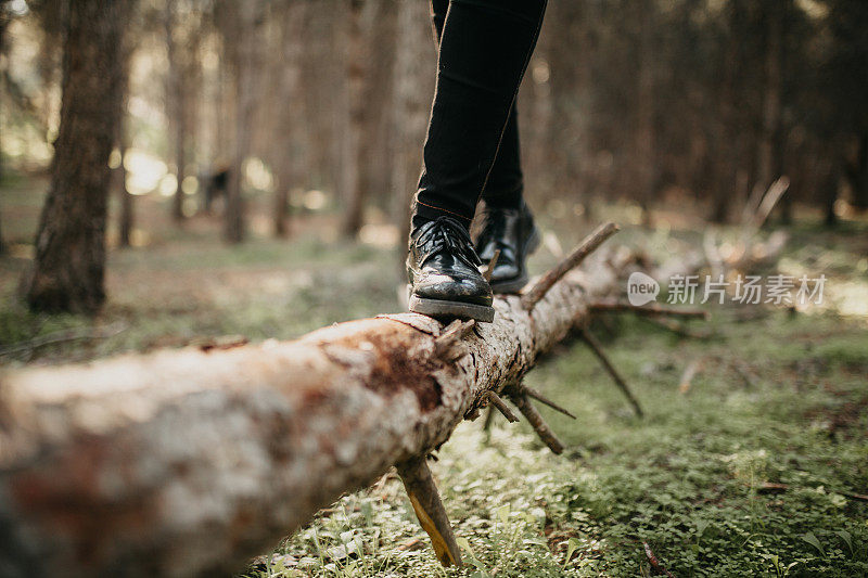穿着黑鞋的脚在倒下的树干上行走，保持平衡。