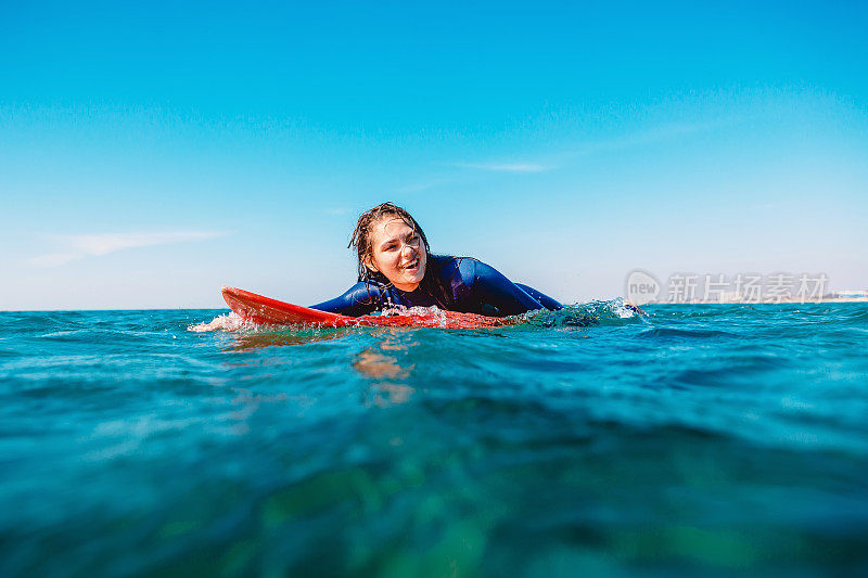 运动冲浪女孩微笑着在冲浪板上划船。在海里带着冲浪板的女人。
