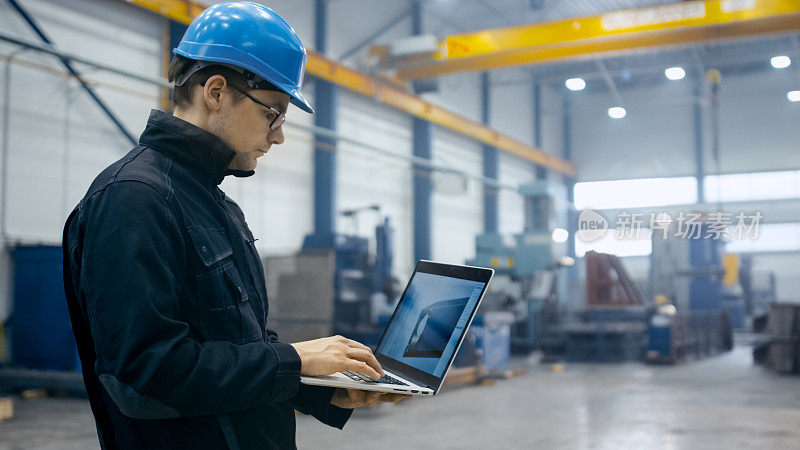 带安全帽的工厂工人正在使用一台装有工程软件的笔记本电脑。