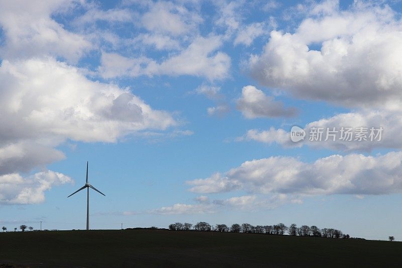 在乡村环境中，蓝天映衬着蓬松的白云，还有风力涡轮机或乡村公路