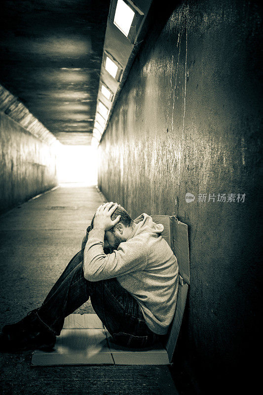 年轻孤独的无家可归的人双手抱头坐在黑暗的地铁隧道里