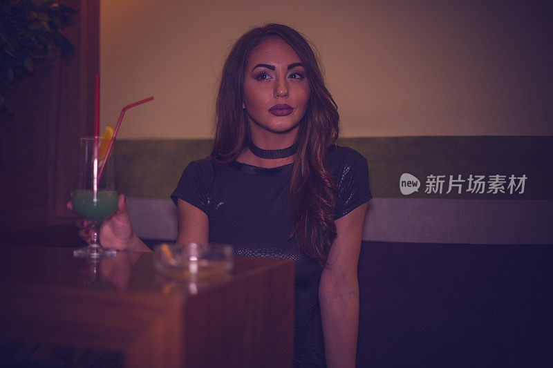 一个年轻漂亮的女人在酒吧喝鸡尾酒的肖像