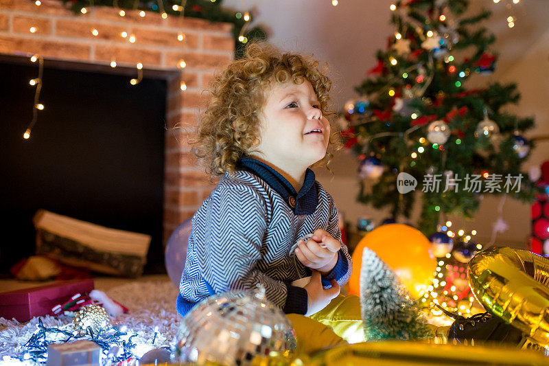 穿着毛衣的漂亮小男孩拿着玩具站在圣诞树前