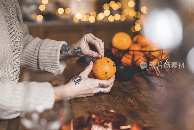 有纹身的女人在圣诞节用丁香装饰橙子
