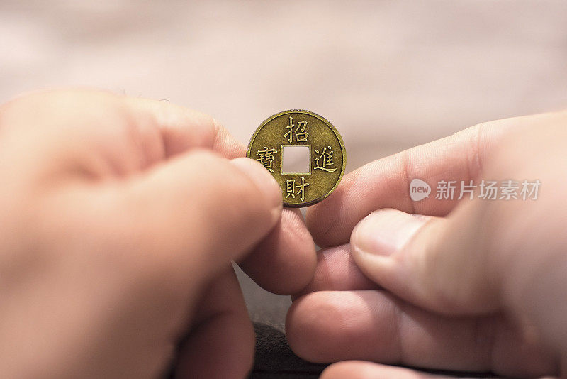 近距离捕捉一个白人男子的手握和旧风水硬币。幸运的中国新年蛋糕硬币。