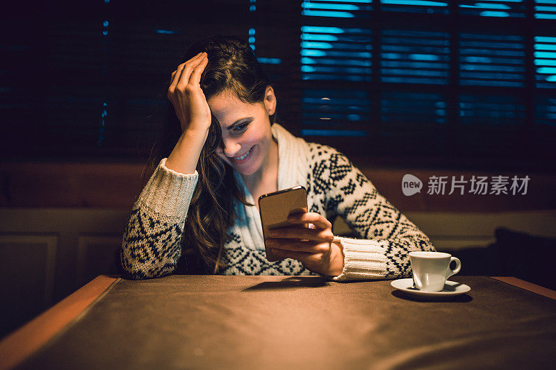 年轻女性喜欢喝咖啡休息时间。她在咖啡馆用手机。