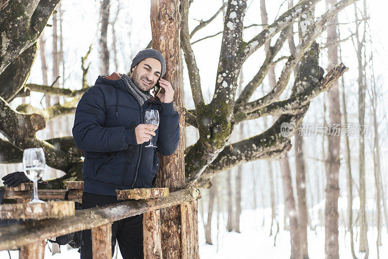 在一个下雪的冬日，一个男人在树林里一边喝酒一边打电话