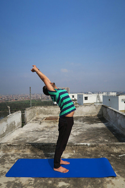 印度人在屋顶上练习举起手臂(Hastauttanasana)瑜伽姿势的照片，德里，印度