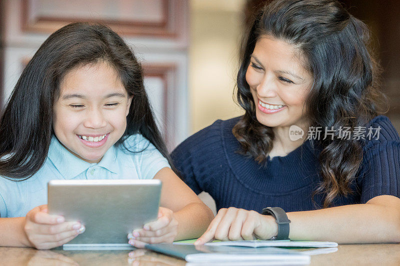 美丽的亚洲妈妈帮助小女孩使用数字平板设备做家庭作业