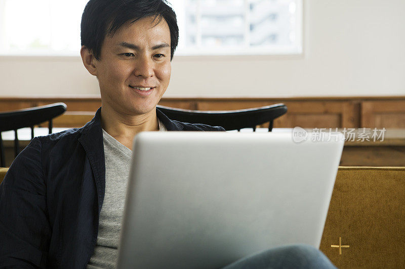 微笑的中年男子在沙发上使用笔记本电脑