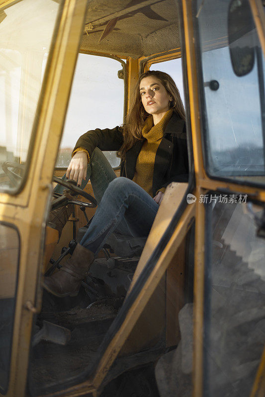 美丽的农妇坐在拖拉机后，在田间工作