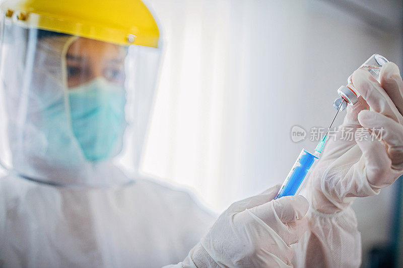 身穿防护服的女医生，手持装有Covid-19病毒冠状病毒疫苗的注射器和导管