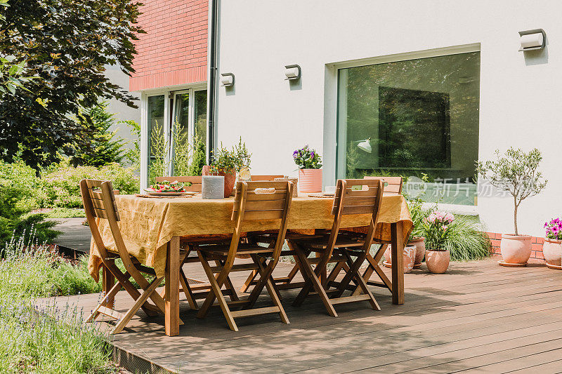 铺着橙色台布的餐桌矗立在绿色花园的木质露台上