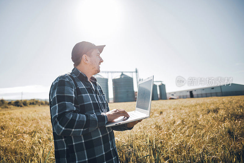 年轻的现代农民在麦田里使用笔记本电脑