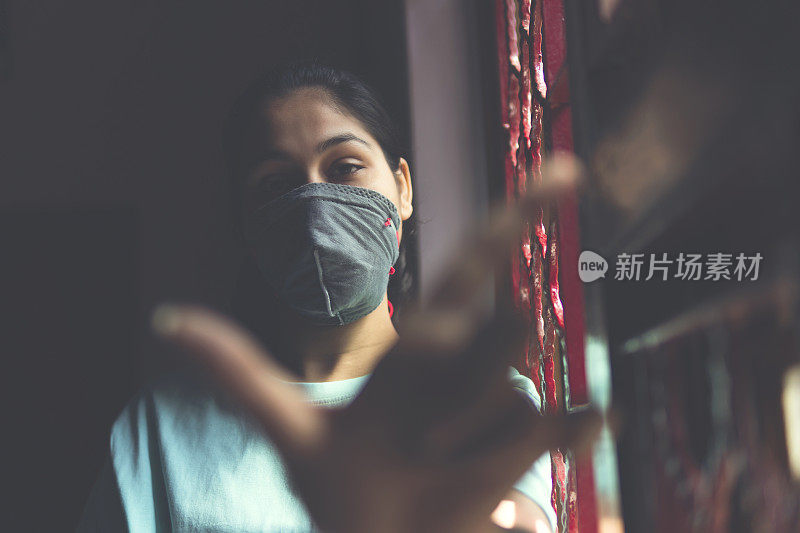 这个悲伤的女孩正在保护自己，戴着口罩，在家里自我隔离。