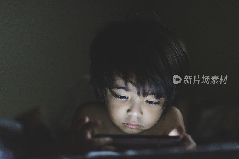 亚洲男孩的肖像，脸被智能手机的屏幕光照亮