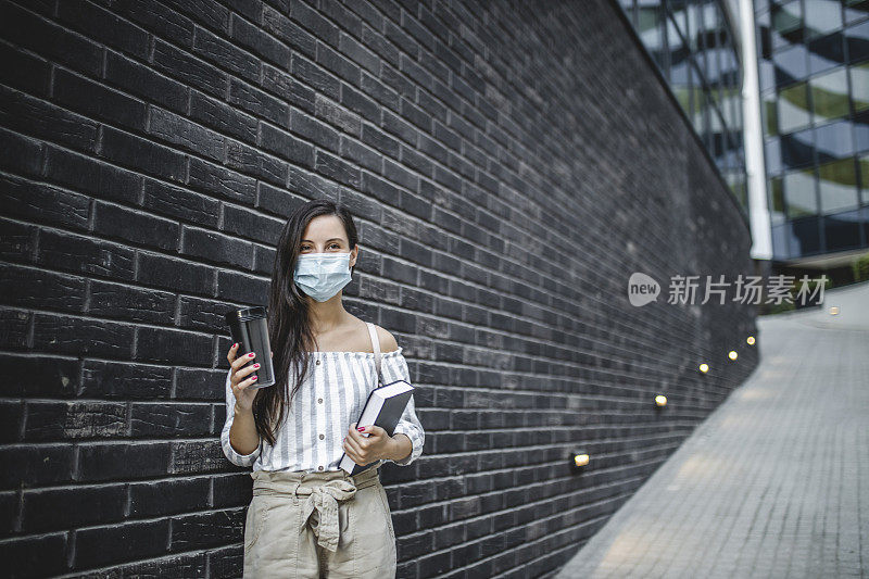 快乐年轻美丽的女学生拿着书和咖啡杯孤立在青砖背景