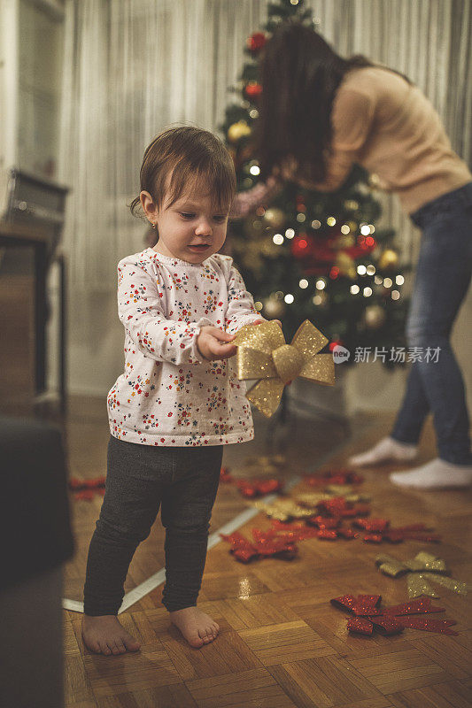 小女孩在她妈妈装饰圣诞树时玩装饰品