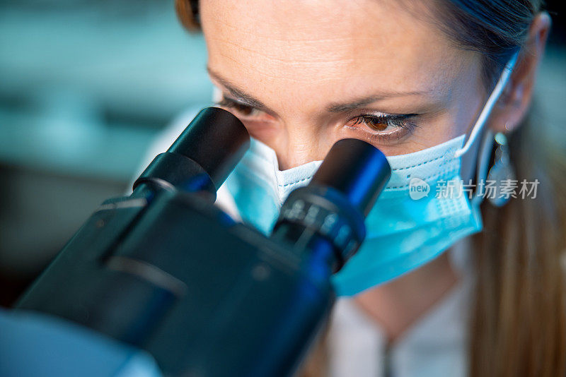 女性微生物学家戴防护面罩，透过显微镜观察