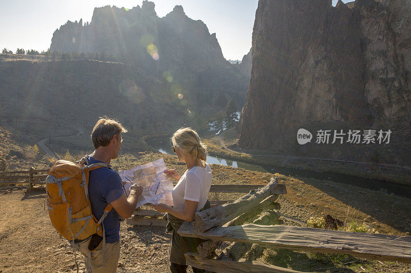 清晨，一对成熟的徒步旅行夫妇在阳光明媚的小径上看地图寻找方向