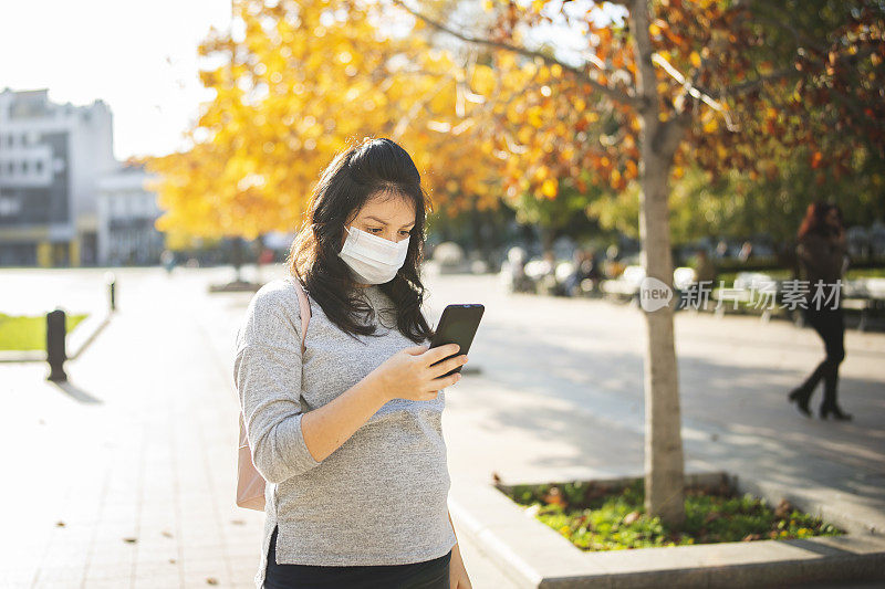 戴着口罩在城市公园里打电话的女人