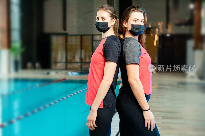 两名妇女戴着医用口罩在游泳池里。专业健身教练在aqua健身房的集体肖像。