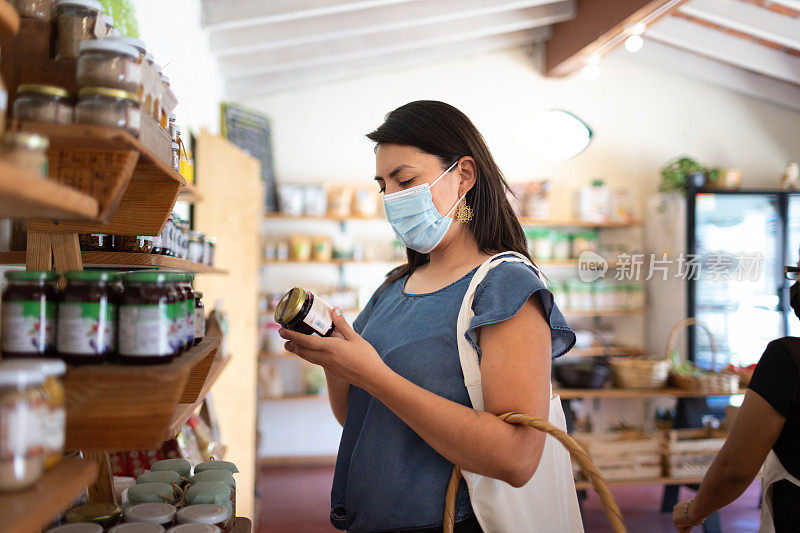 新常态:戴着防护口罩的年轻女性在当地的小商店购买有机食品