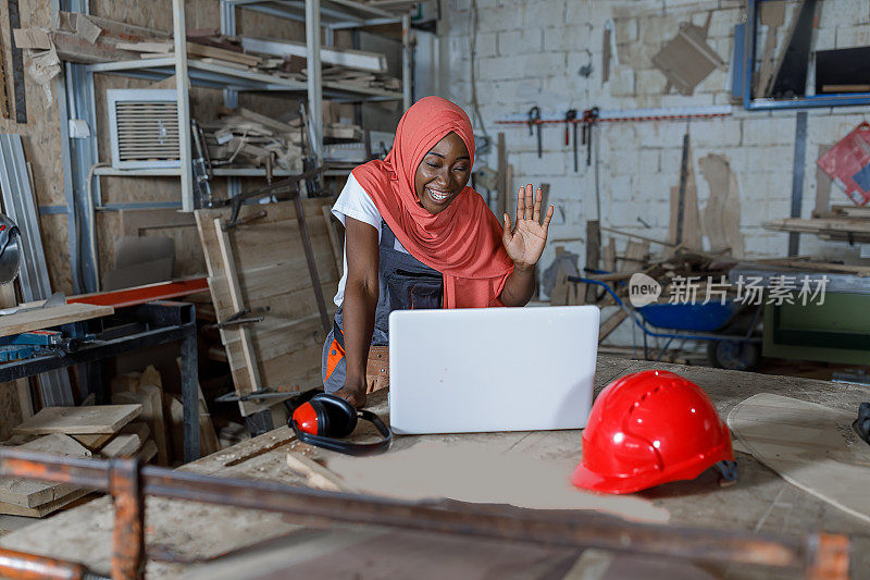 一名穆斯林女木匠在生产车间工作，同时使用笔记本电脑进行在线学习。