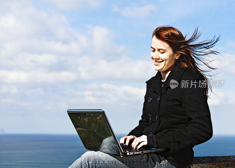 年轻的红头发，在悬崖顶上用笔记本电脑俯瞰大海，微笑着