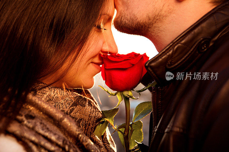 多情的小伙子用红玫瑰轻轻吻着他的女孩