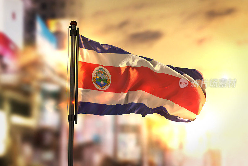 哥斯达黎加国旗对城市模糊的背景在日出背光