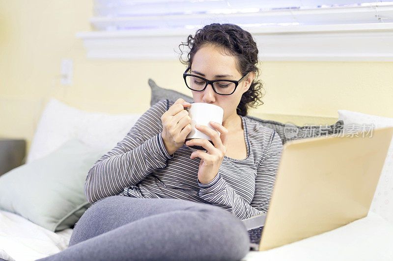 年轻女性一边喝茶一边用笔记本电脑