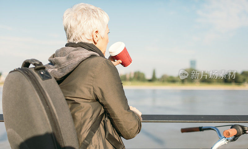 站在河边喝咖啡的成熟女人。