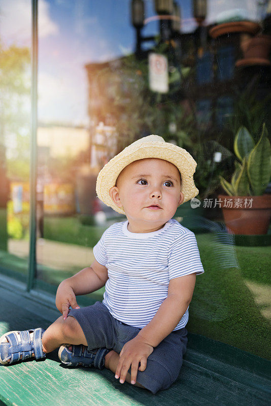 表情丰富的都市小男孩坐在商店橱窗旁。