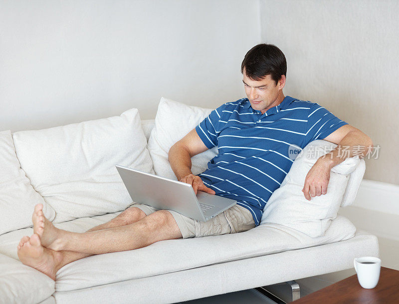 一个成熟的男人在沙发上放松的时候用着笔记本电脑