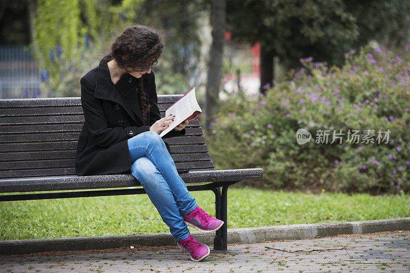 年轻女子在公园长椅上看书